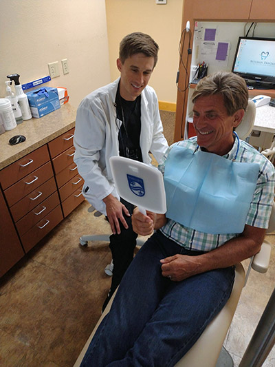 man smiling in mirror after cosmetic dentistry treatments in Bedford, TX
